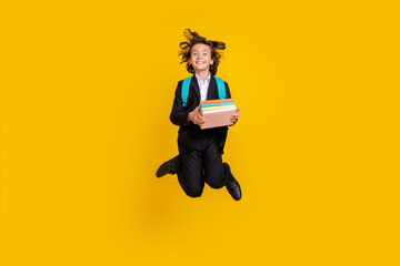 Photo of a-student schoolboy hold stack book jump wear bag black uniform isolated yellow color background
