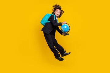 Fototapeta na wymiar Photo of shocked surprised little boy jump hold globe wear rucksack black uniform isolated yellow color background