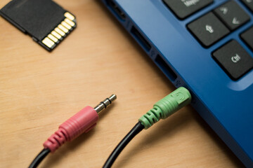 Earphones cables connected to a blue modern laptop, USB memory  and SD memory on a wooden table 
