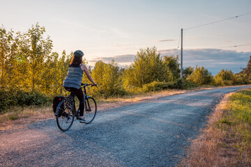 Adventurous White Cacasusian Woman riding a bicycle on a road. Sunny Summer Sunset. Barnston Island, Vancouver, British Columbia, Canada. Adventure Journey Concept