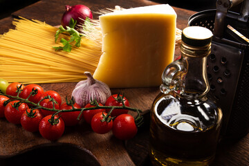 Italian pasta (macaroni), spaghetti, tomatoes, olive oil, cheese and spices on rustic wood, selective focus.