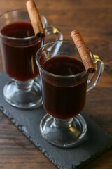 Mulled wine in glass cups with cinnamon and oranges on a wooden table.