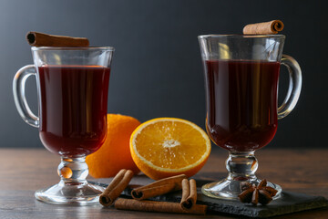 Mulled wine in glass cups with cinnamon and oranges on a wooden table.