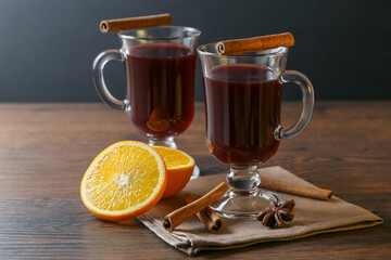 Mulled wine in glass cups with cinnamon and oranges on a wooden table.