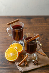 Mulled wine in glass cups with cinnamon and oranges on a wooden table.