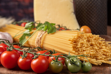 Italian pasta (macaroni), spaghetti tied with sisal string, tomatoes, olive oil, cheese and spices on rustic wood, selective focus.