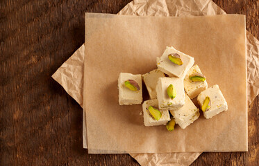 Natural vegan product. Halva with pistachios on parchment paper on a wooden background. Turkish, Arab and Jewish national sweets. Traditional oriental dessert Chekme. Copy space