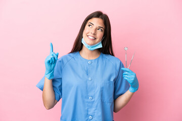 Dentist woman holding tools isolated on pink background pointing up a great idea