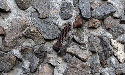 A metal rusty old bolt embedded in the wall along with stones. Abstract background with stones and bolt