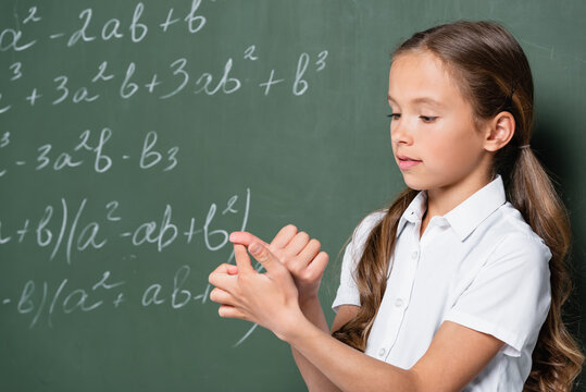 Preteen Schoolgirl Counting On Fingers Near Chalkboard With Mathematic Equations