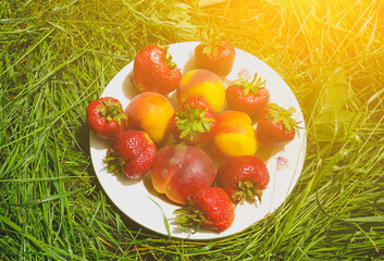 Strawberries and peaches on a plate on the green grass. Delicious and fresh summer fruits. Healthy...