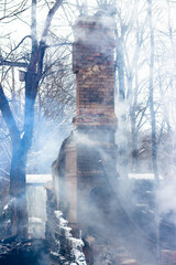 Remains of a house after a fire. The brick tube of the stove is shrouded in dense smoke