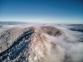 Aerial view, sea of fog and slope illuminated by the rising sun, snow on the tops of the mountains. Russia