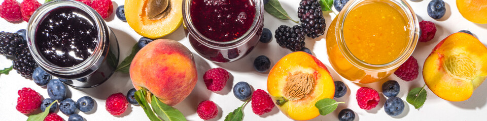 Assortment of summer seasonal berry and fruits jams in small jars, homemade preserving concept, marmalades or confitures with fresh berries on white background copy space