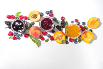 Assortment of summer seasonal berry and fruits jams in small jars, homemade preserving concept, marmalades or confitures with fresh berries on white background copy space