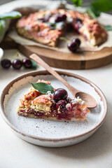 Piece of open pie or galette with cherry, almond and vanilla ice cream, light background.