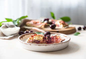 Piece of open pie or galette with cherry, almond and vanilla ice cream, light background.