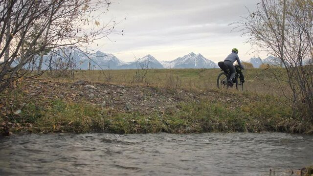 The woman travel on mixed terrain cycle touring with bikepacking. The traveler journey with bicycle bags. Sportswear in green black colors. The trip in magical autumn forest, river stream.