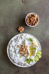 Traditional bulgarian cold summer soup tarator with ingredients on green background. Bulgarian soup with grated cucumbers, yogurt and walnuts. Top view.