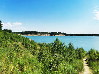 Fototapeta na wymiar Beautiful blue lake surrounded by forest. Grass and flowers by the lake in a sandy quarry