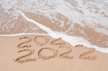 Inscription 2021 and 2020 numbers written on sand.  New Year 2022 replace 2021. Concept on the sea beach