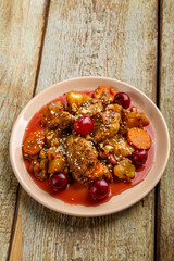 Jewish dish stewed potatoes with chicken in cherry sauce decorated with cherries on the table in a plate.
