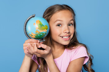 Schoolchild holding globe and looking at camera isolated on blue