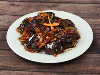 Veg Manchurian, Popular indo-chinese food made of cauliflower florets and other vegetable, served in a white plate over a rustic wooden table. selective focus