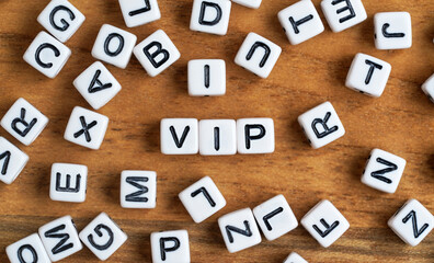 Small white and black bead cubes on wooden board, letters in middle spell VIP - Very important person concept