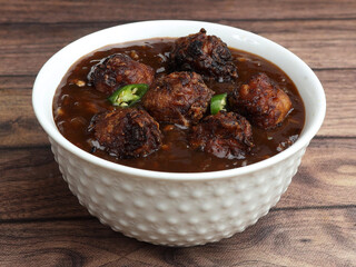 Veg Manchurian, Popular indo-chinese food made of cauliflower florets and other vegetable, served in a white plate over a rustic wooden table. selective focus