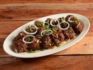 Veg Manchurian, Popular indo-chinese food made of cauliflower florets and other vegetable, served in a white plate over a rustic wooden table. selective focus