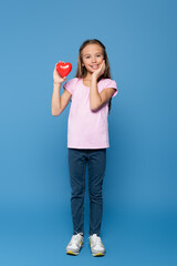 Girl holding red decorative heart on blue background