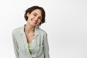 Obraz premium Portrait of beautiful brunette woman, girl smiling white teeth and looking happy, posing tenderly, standing in shirt over white background