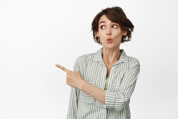 Portrait of surprised young woman pucker lips curious, pointing and looking left at interesting...