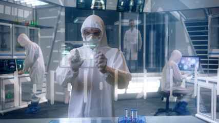 Inside Quarantine Secure High Level Laboratory Scientists in a Coverall Conducting a Research Analyzing Virus DNA Structure using Transparent Display Tablets and Modern Technology.
