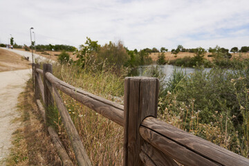 Fototapeta premium Brown wooden fence with a pond in the background on a park path