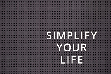 Phrase Simplify Your Life spelled out with white letters on gray pegboard