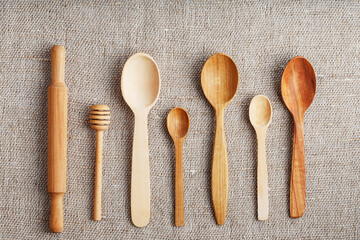 Craft spoons made from different types of wood lie in a row on a hemp burlap fabric. Top view, free space