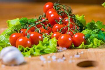 Fresh cherry tomatoes with green salad and garlic on a cutting board.