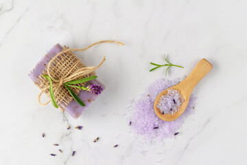 Lavender soap, violet salt on wooden spoon and  fresh flowers on white marble background. Bath body care or spa wellness concept.
