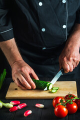 Cook or chef cuts a green cucumber on a restaurant kitchen cutting board for salad. Vegetable diet or snack idea.