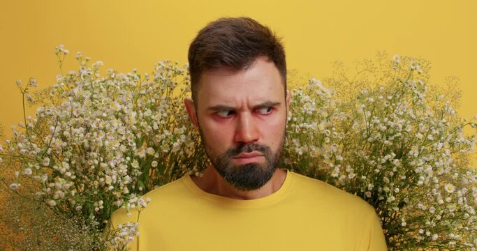 I want allergy free life. Irritated bearded Caucasian man tries to get out of allergen surrounded by wildflowers looks angrily at camera isolated over yellow background. Health problems concept
