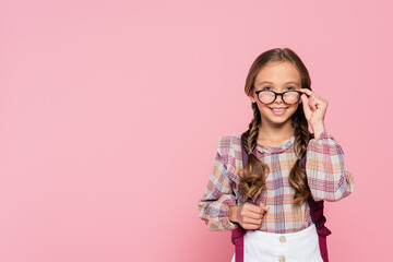 Fototapeta Positive schoolgirl holding eyeglasses isolated on pink obraz