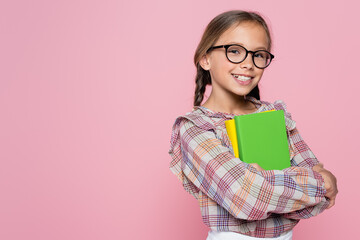 cheerful girl with textbooks smiling at camera isolated on pink