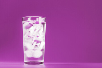 Glass with water and ice cubes on a pink background