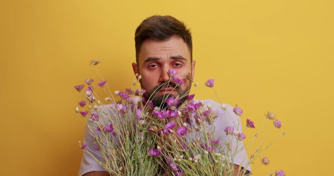 Allergic man has shortness of breath surrounded by wildflowers causing allergy suffers from suffocation keeps hands on neck poses against yellow background. Asthmatic fit hypersensitivity concept