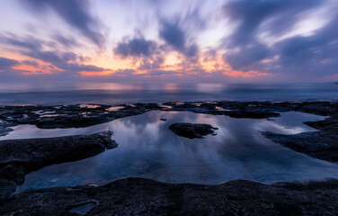 Naklejka premium amazing scenic view at a sea shore from a coast after dramatic colorful sunset with flying blured clouds and reflection on water surface , beautiful ocean landscape