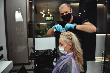 A hairdresser stylist in medical mask highlighting a strand of hair of a woman during hair dyeing