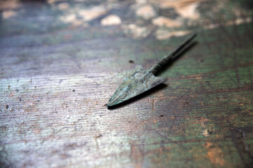 Close up of an undated arrowhead, made of bronze, oxidized color on similar color wooden surface...