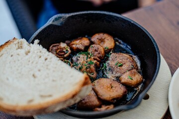 Frying pan of fresh mushrooms and a slice of bread on a wooden board.